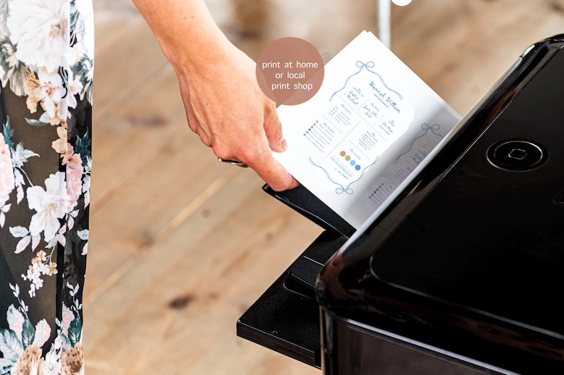 May include: A white rectangular paper document with blue text and a decorative border being fed into a black printer. The document features the text 'print at home or local print shop' in a circular brown speech bubble overlaying the paper.