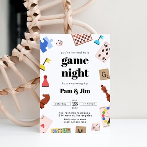 May include: A white invitation card with colorful illustrations of board games and the text "you're invited to a game night housewarming for Pam & Jim Saturday May 23 at 4:00pm 20XX the reynolds residence 1234 main st, los angeles kindly rsvp to emma (345) 567.890.7654"