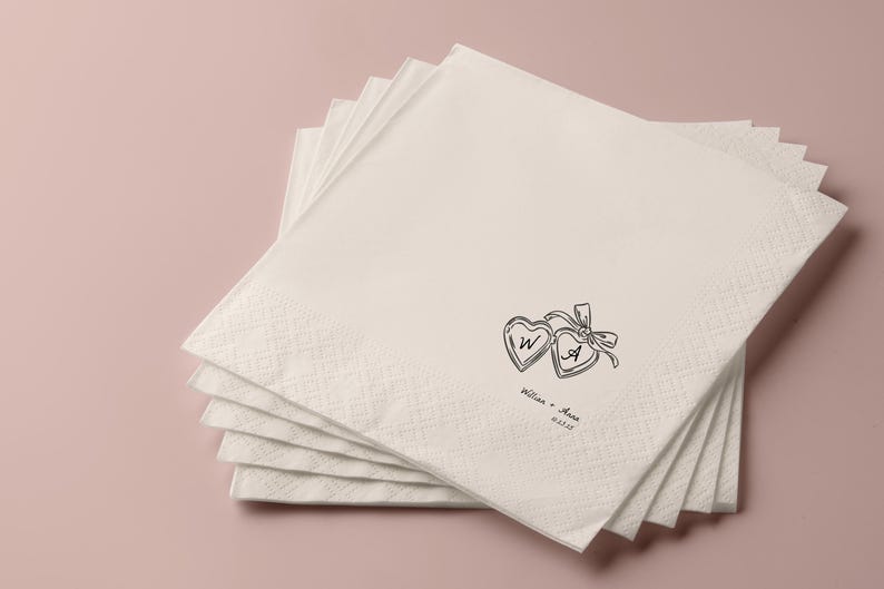 May include: A stack of off-white paper napkins with a subtle diamond pattern. Each napkin is decorated with a black line drawing of two hearts tied with a bow, with the initials "W" and "A" inside. The names "William & Anna" and a date are printed below.