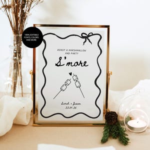 May include: A framed sign with the text "Roast a Marshmallow and Party S'more" in black script. The sign includes a drawing of marshmallows on sticks and the names "Sarah + Jason" with the date "22.04.25". The frame is gold.