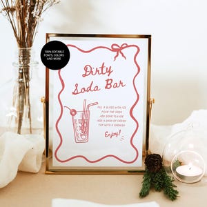 Op de afbeelding: Een goudkleurig ingelijst bord met de tekst "Dirty Soda Bar" in rode letters. Het bord bevat instructies voor het maken van een frisdrank, een tekening van een frisdrank en het woord "Enjoy!"