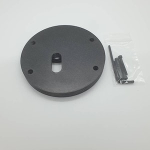 Puede incluir: Una base circular negra con una ranura en el centro y cuatro agujeros para tornillos alrededor del borde. Se incluye una pequeña bolsa de tornillos.