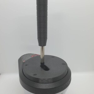 May include: Black shifter with a textured black knob and a silver metal shaft. The shifter has a circular base with a textured surface and several small screws.