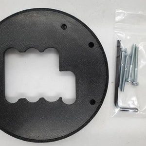 May include: A black, circular component with a gear shift pattern cut out, featuring multiple mounting holes. A clear plastic bag contains several silver bolts and an Allen wrench, likely for installation. The item appears to be a replacement part.