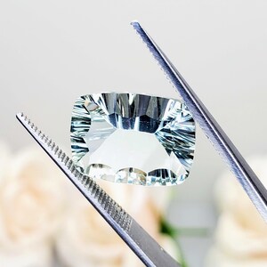 May include: A light green gemstone with a faceted cut, held by tweezers. The gemstone has a rectangular shape and is transparent.
