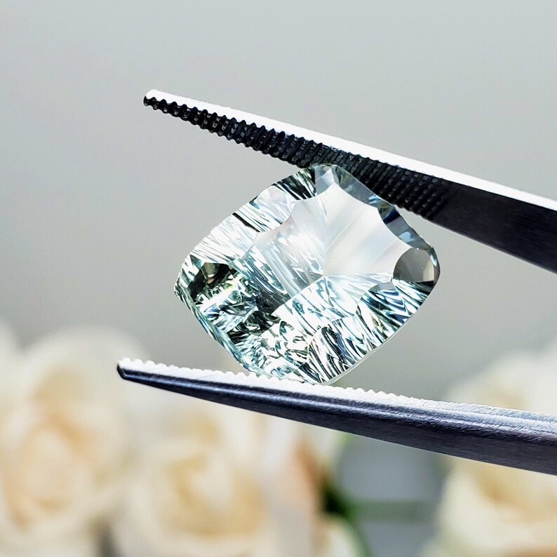 May include: A light green gemstone with a faceted cut, held by tweezers. The gemstone has a unique, striated pattern.