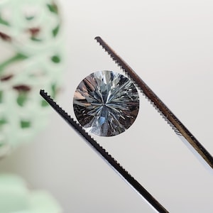 May include: A clear, faceted gemstone with a star-like pattern held by tweezers.