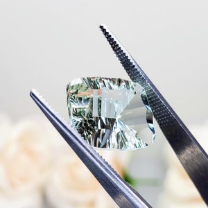 May include: A light green gemstone with a faceted cut, held by tweezers. The gemstone has a unique, striated pattern.