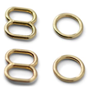 May include: Four gold-colored metal hardware pieces. Two are figure-eight shaped, and two are circular rings. The items are displayed on a white background. These findings are likely used in crafting or jewelry making.