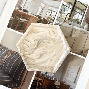 May include: A hexagonal tray featuring a marbled pattern with swirling shades of cream, beige, and light gray. The tray has a smooth, polished surface with raised edges and a distinct geometric shape, showcasing a neutral color palette throughout.