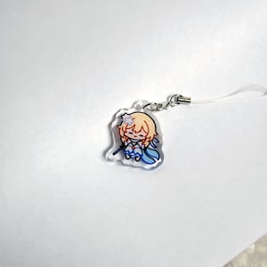 May include: A clear acrylic charm depicting a cartoon character with blonde hair, blue and white clothing, and a small wand. The charm has a silver-coloured clasp and a white lanyard. The design is a chibi-style illustration.