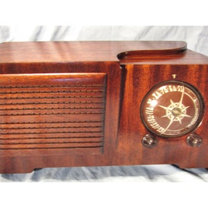 May include: A vintage wooden radio with a round dial and a speaker grille. The radio is made of dark wood and has a brown finish.