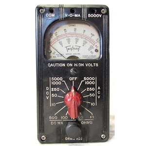 May include: A vintage black Triplett V-O-MA multimeter with a red knob and a circular gauge. The gauge displays ohms, DC, and AC voltage readings. The text "CAUTION ON HIGH VOLTS" is visible.