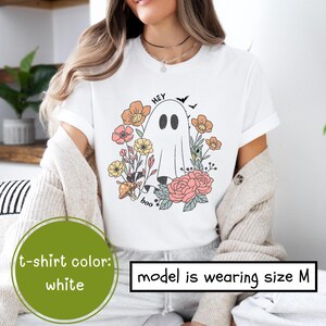 May include: White t-shirt with a ghost and flowers graphic. The text "Hey Boo" is printed on the shirt. The model is wearing size M.