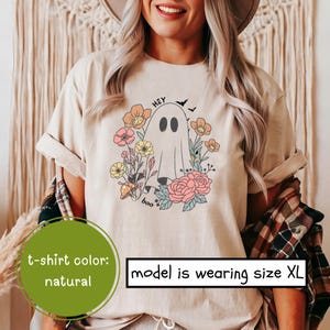 May include: A beige t-shirt with a graphic of a ghost surrounded by flowers. The text "Hey Boo" is printed on the shirt.