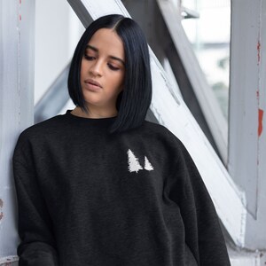 Pode incluir: Camisola de moletom preta com um desenho bordado branco de duas árvores de pinho.