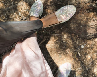 Op de afbeelding: Een paar glinsterende zilveren loafers met een spitse neus. De loafers zijn bedekt met strass en hebben een lichtbruine leren zool.