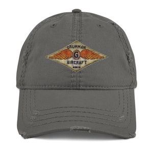 May include: A gray distressed baseball cap with a vintage Grumman Aircraft logo featuring a winged G in a diamond shape. The logo is in orange, yellow, and blue.