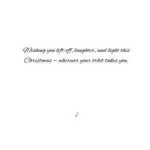 May include: A white card with elegant cursive text. The text reads: "Wishing you lift-off, laughter, and light this Christmas - wherever your orbit takes you." A small checkmark is at the bottom.