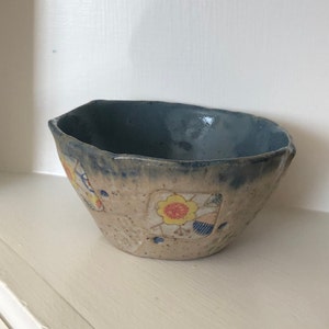 May include: A small, blue and white ceramic bowl with a floral design. The bowl has a rough, textured surface and a slightly uneven rim.