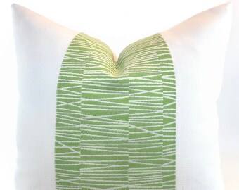 Può includere: Cuscino quadrato bianco con un pannello verticale centrale in tessuto verde chiaro. Il pannello verde presenta un motivo di linee bianche, orizzontali e leggermente angolate. Un elemento decorativo per la casa.