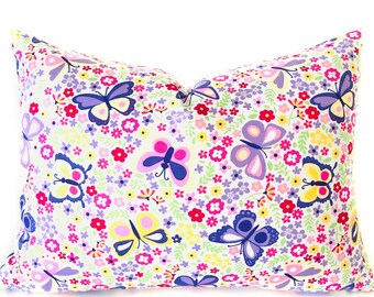May include: A rectangular pillow with a white background covered in a pattern of colorful butterflies and small flowers. The butterflies are in shades of purple, pink, and yellow, while the flowers are red, purple, and yellow. The pillow is designed for decorative use.