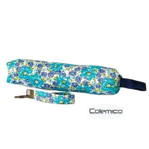 May include: A floral print pencil case and matching wristlet. The pencil case is a long, cylindrical shape with a navy blue handle. The wristlet has a metal clasp. Both items feature a white background with turquoise and blue flowers.