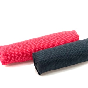 May include: Two cylindrical pillows. One is red with white polka dots, and the other is dark blue with a repeating geometric pattern. The pillows are side by side against a white background.