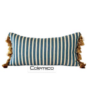 May include: A long, rectangular pillow with blue and white stripes and gold tassels on each end. The pillow is made of a soft, woven fabric.