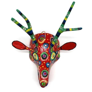 May include: A vibrant, handcrafted deer head wall hanging. The red base is adorned with colorful, circular patterns. The antlers are green with blue and yellow stripes, and the ears are red. A unique piece of folk art.