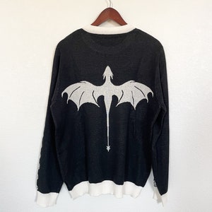 May include: Black long-sleeved sweater with a white dragon design on the back. The sweater has a white ribbed collar and cuffs.