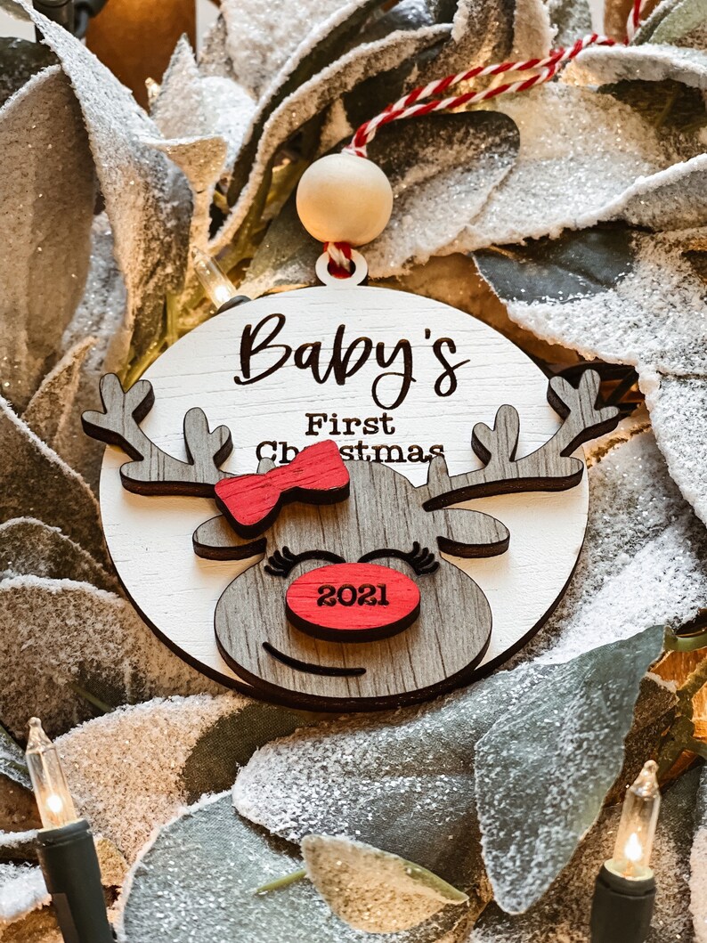 May include: A wooden reindeer ornament with a red bow and the text "Baby's First Christmas 2021".