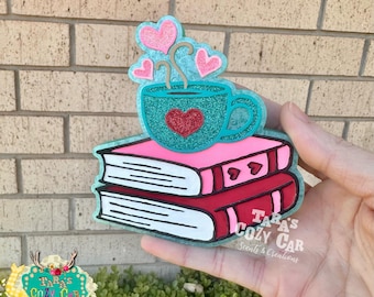 May include: A teal glittery coffee cup with a red heart sits atop two books. Pink hearts float above the cup. The books are pink and red with white pages. The text "Tara's Cozy Car" is visible.