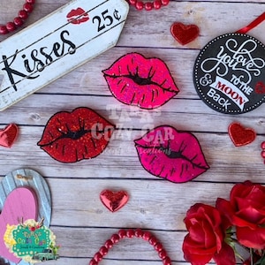 May include: A collection of Valentine's Day themed decorations. The image features three glittery lip-shaped ornaments in red and pink, along with heart-shaped accents, a wooden sign that says "Kisses", and a round sign that says "Love you to the moon & back".