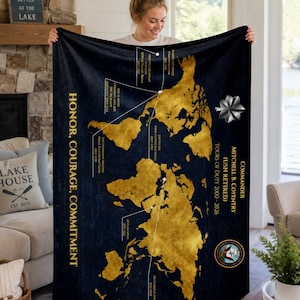 May include: A navy blue blanket with a gold world map design. The blanket features text that reads "Honor, Courage, Commitment" and "Commander Mitchell B. Coventry (USN Retired)". The blanket is held up by a person.