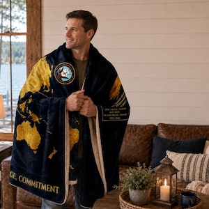 May include: A navy blue and gold blanket featuring a world map design. The blanket has a cream-colored border and a patch with text and an emblem. The words "Courage, Commitment" are printed on the blanket.
