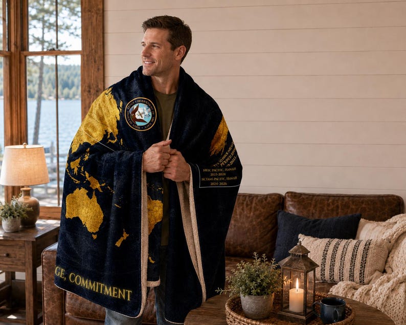 May include: A navy blue and gold blanket featuring a world map design. The blanket has a cream-colored border and a patch with text and an emblem. The words "Courage, Commitment" are printed on the blanket.