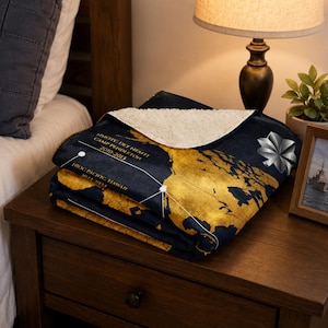 May include: A navy blue and gold map-themed blanket with white text and a white sherpa lining. The blanket features a world map design with text that reads "NMOTC DET NEMTI CAMP PENDLETON 2010-2013" and "NIOC PACIFIC HAWAII 2022-2024".