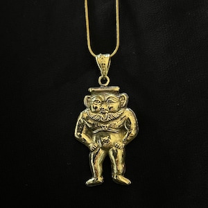 Może przedstawiać: Złoty naszyjnik z wisiorkiem przedstawiającym stylizowaną postać w kapeluszu z rękami po bokach. Wisiorek wisi na cienkim, złotym łańcuszku na czarnym tle. Postać ma uśmiechniętą twarz i stoi.