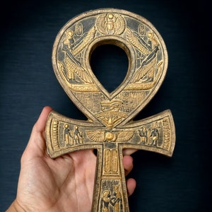 May include: A detailed, gold-colored Ankh symbol with intricate hieroglyphic carvings and a dark background. The Ankh, an ancient Egyptian symbol of life, features a loop at the top and a cross-like shape below, with detailed relief carvings.