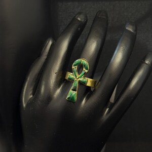 Puede incluir: Un anillo de oro con un símbolo Ankh de esmalte verde y negro.