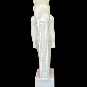 May include: White stone statue of an Egyptian god with hieroglyphics on the front. The statue is standing on a square base.