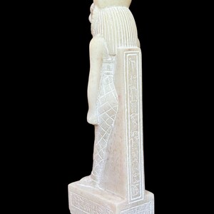 May include: White alabaster statue of an Egyptian god with hieroglyphics on the base and side. The statue is standing on a rectangular base.