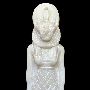 May include: White alabaster statue of the Egyptian goddess Bastet, depicted as a woman with a lion's head wearing a crown and a necklace.