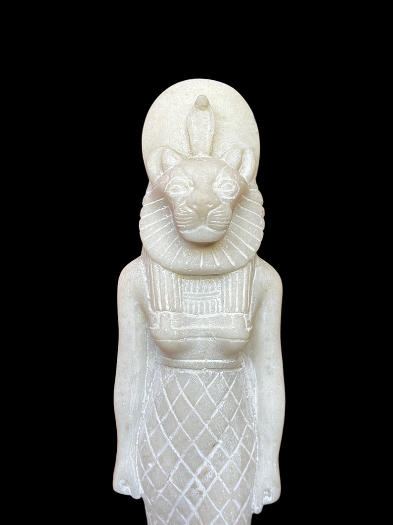 May include: White alabaster statue of the Egyptian goddess Bastet, depicted as a woman with a lion's head wearing a crown and a necklace.