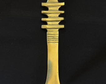 Może przedstawiać: Złoty metalowy ornament w kształcie pagody z ostrym wierzchołkiem i płaską podstawą.