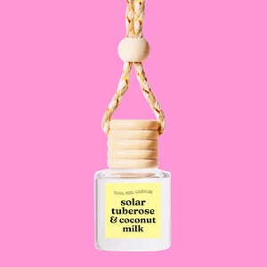May include: A clear glass bottle with a wooden lid and a string for hanging. The bottle contains a car air freshener with the text "COOL GIRL CANDLES solar tuberose & coconut milk".