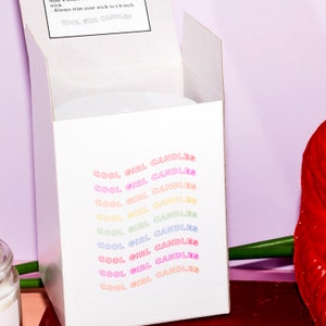 Puede incluir: Caja de cart&oacute;n blanca con las palabras "COOL GIRL CANDLES" repetidas en colores arco&iacute;ris en la parte delantera.