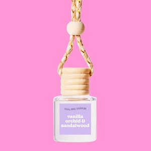 Peut inclure: Une bouteille en verre transparente avec un bouchon en bois et une ficelle pour l'accrocher. La bouteille porte une étiquette qui dit "Cool Girl Candles" et "vanilla orchid & sandalwood".
