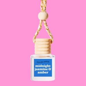 May include: A clear glass bottle with a wooden cap and a blue label that reads "Cool Girl Candles midnight jasmine & amber" hanging from a beige and gold rope.